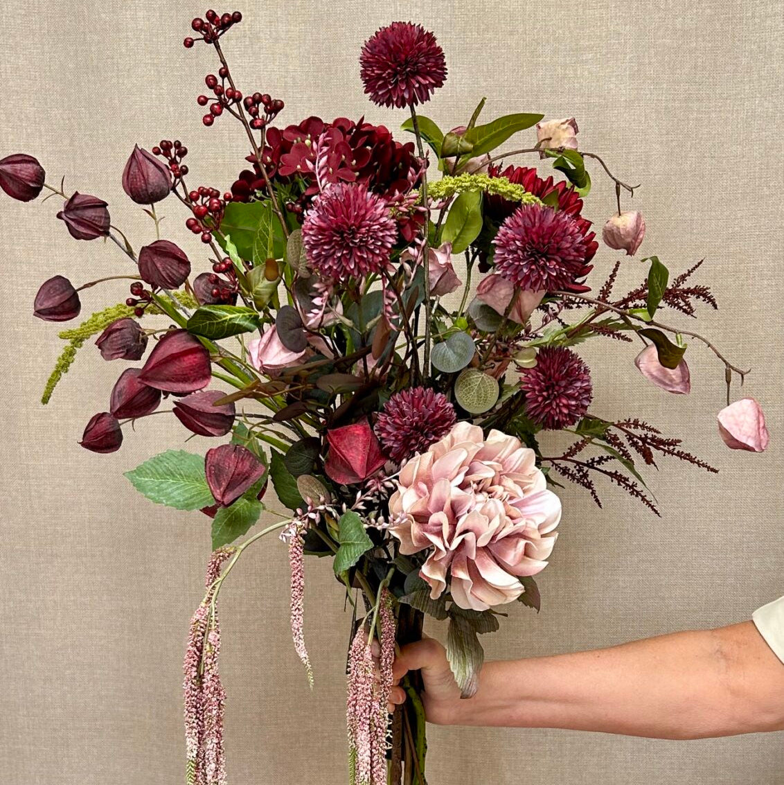 Bordeaux hortensia i en håndholdt buket med rosa og vinrøde kunstige blomster