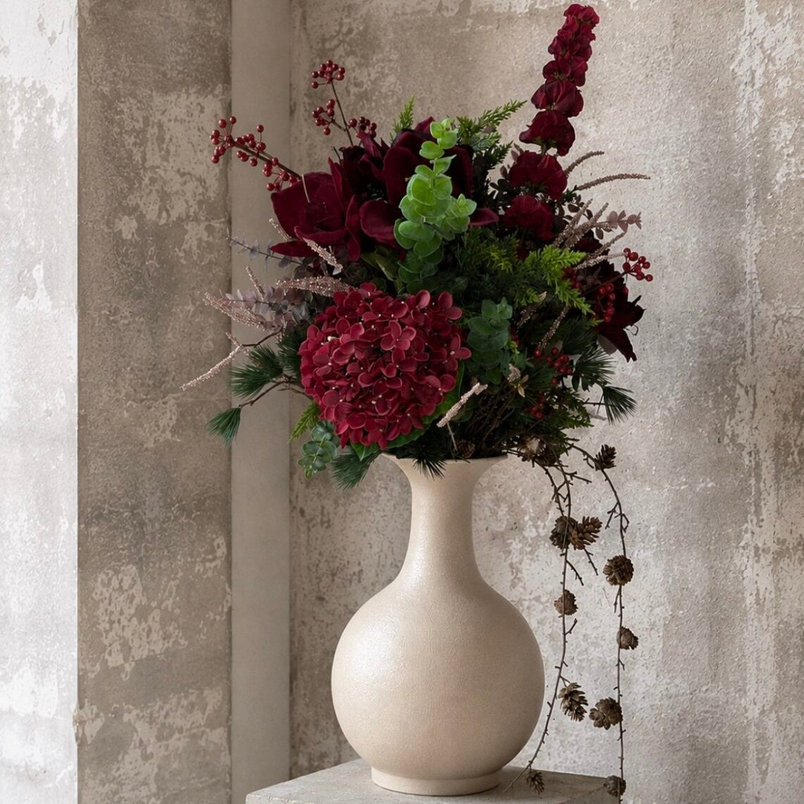 Bordeaux hortensia i en blandet buket med bær og grønne grene i en lys vase